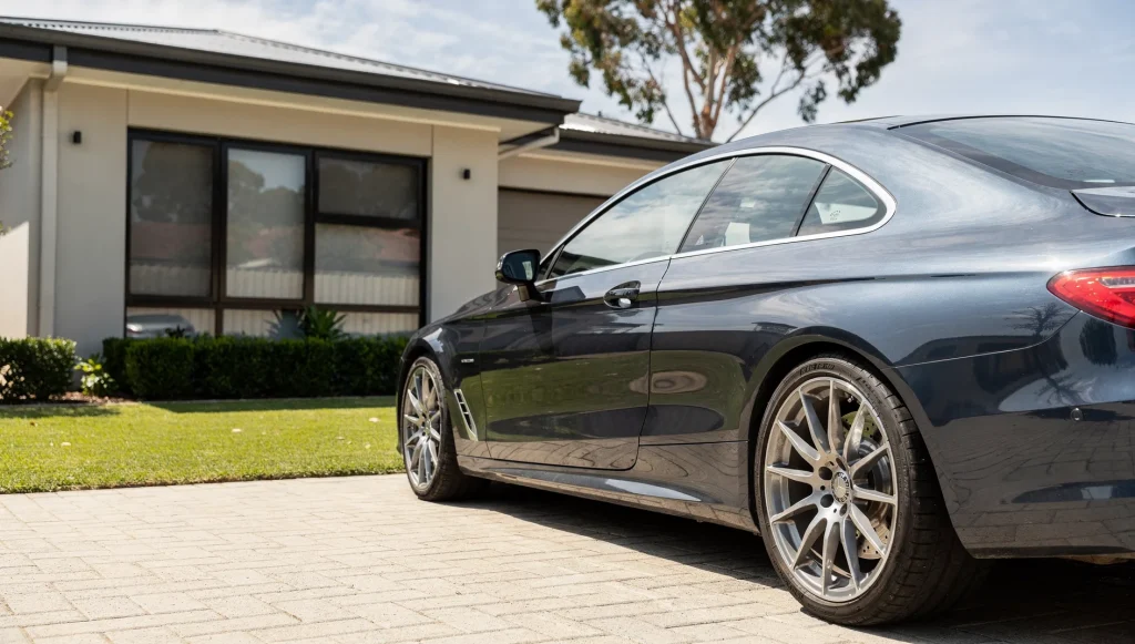 Freshly detailed metallic-graphite Mercedes-Benz saloon on clean concrete outside an O'Connor brick home.