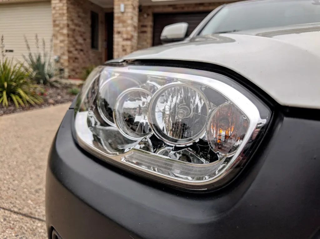 Restored crystal-clear headlight lens with sharp chrome reflectors after O'Connor car detailing.