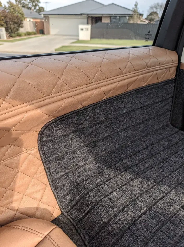 Detailed diamond-quilted leather seat bolster beside vacuumed carpet after O'Connor car detailing.