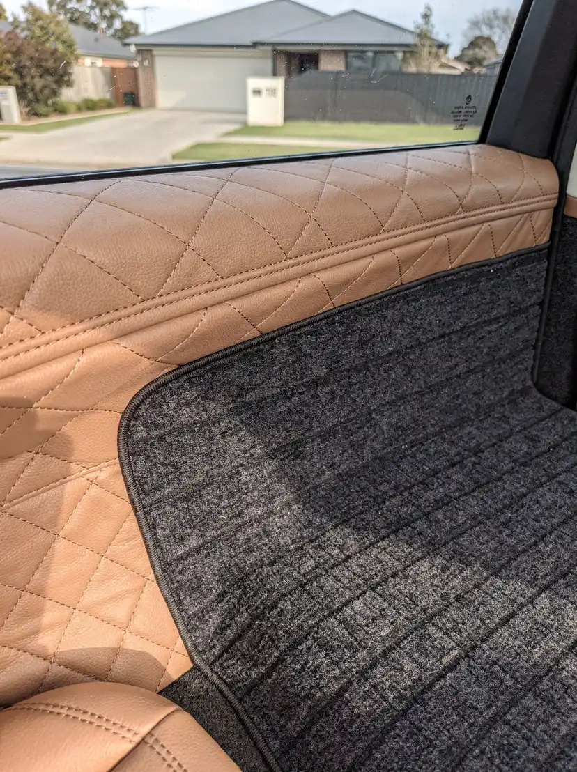 Detailed diamond-quilted leather seat bolster beside vacuumed carpet after O'Connor car detailing.